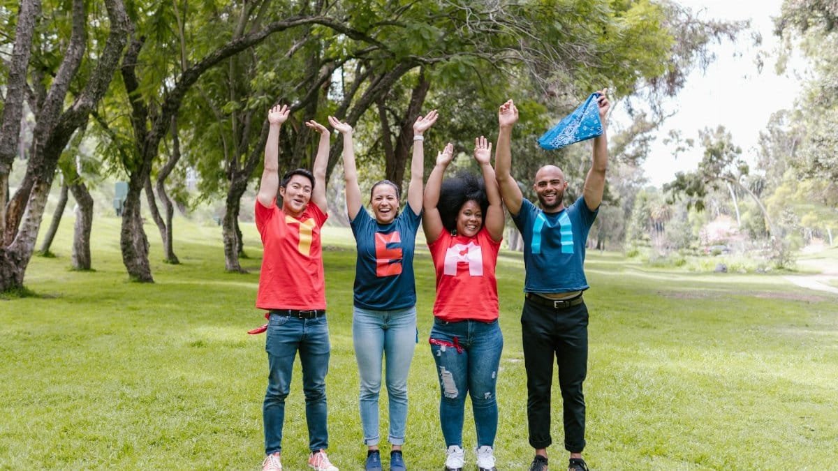 A joyful group of diverse adults celebrating teamwork outdoors in a lush, green park.