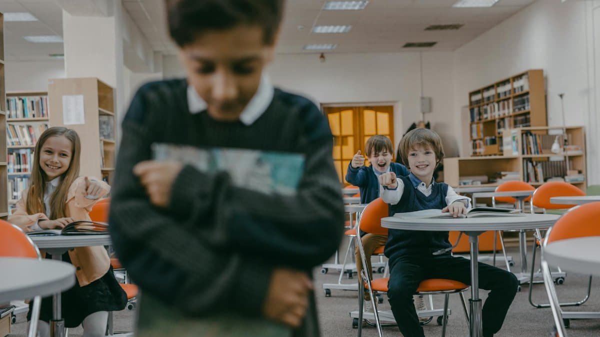 A group of children laughing and pointing at a sad classmate in a school library.
