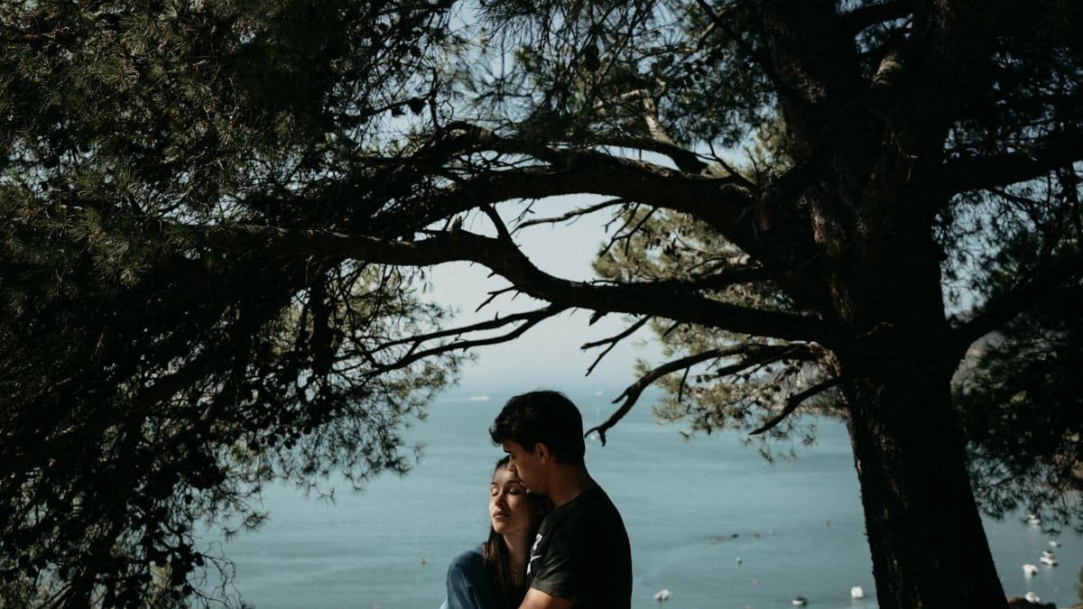 A couple embracing under trees with a scenic ocean view, conveying love and tranquility.
