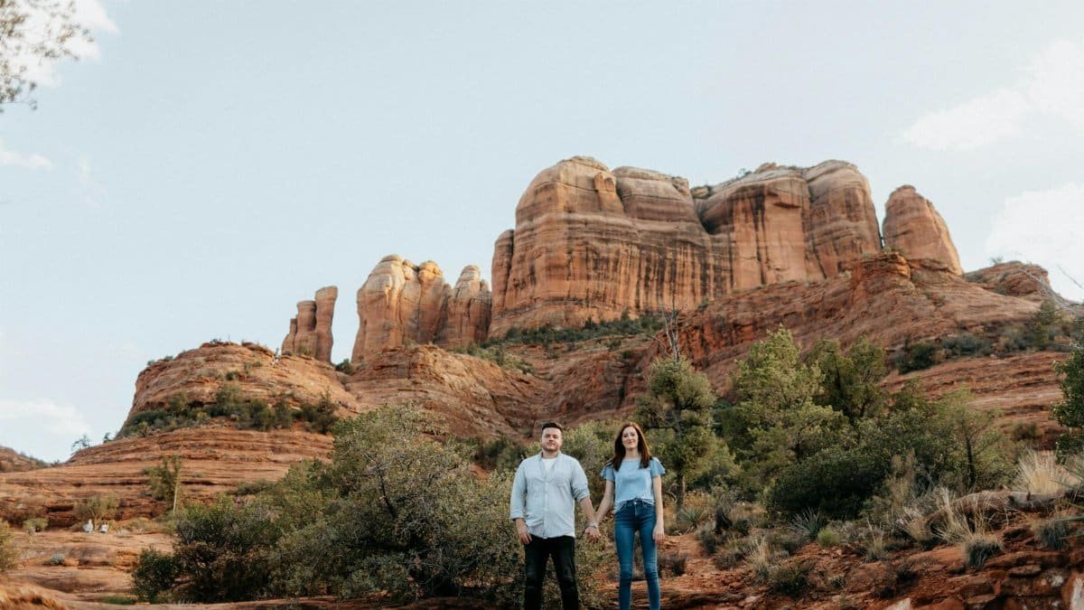 A couple stands in front of the stunning Cathedral Rock in Sedona, Arizona, capturing a serene outdoor moment.