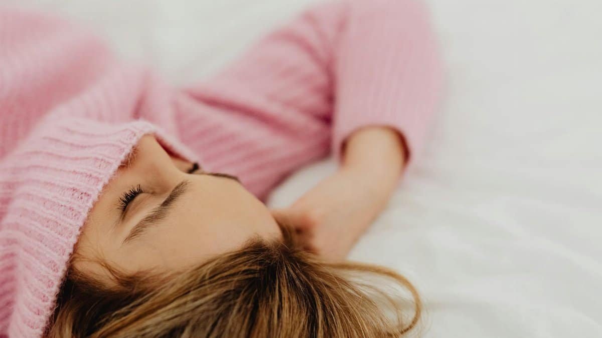 A serene image of a woman sleeping peacefully in a cozy pink sweater on a white bed.