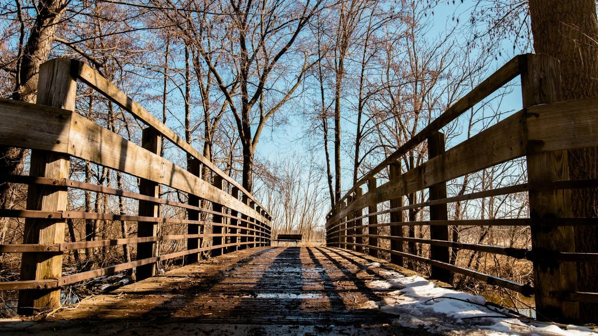 A picturesque wooden bridge in a snowy winter setting, surrounded by bare trees in Ann Arbor, Michigan.