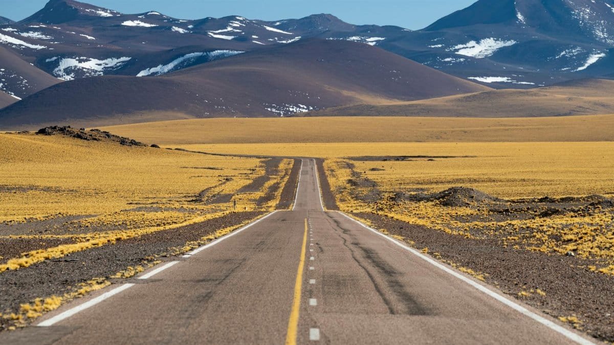 A long road stretches through a barren desert landscape with mountains in the distance.