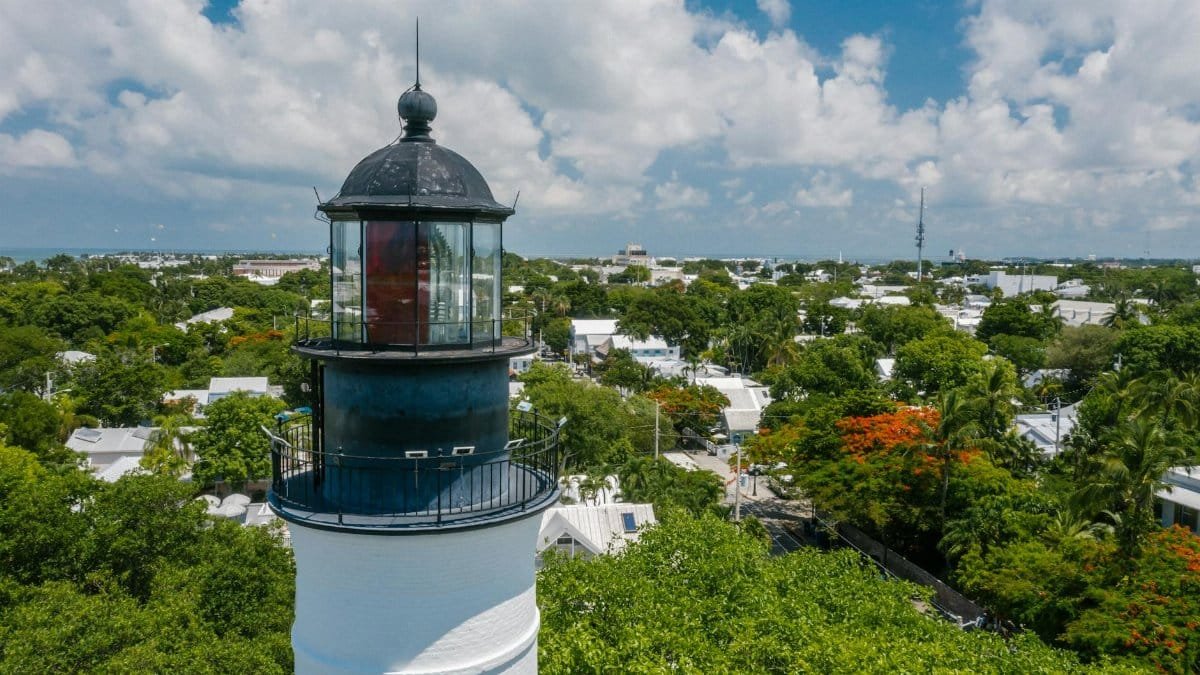Discover the historic Key West lighthouse surrounded by lush greenery under a bright blue sky.