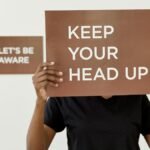A motivational sign reading 'KEEP YOUR HEAD UP' held by a person indoors.