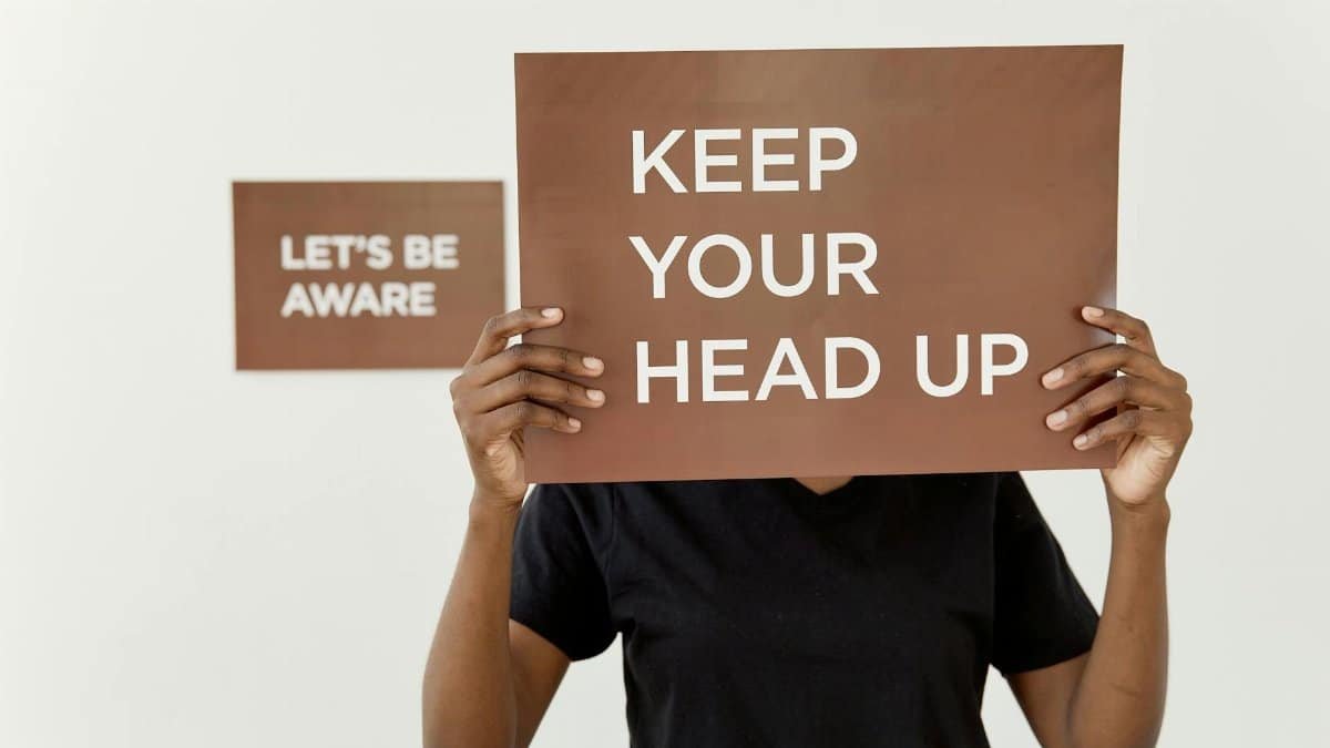 A motivational sign reading 'KEEP YOUR HEAD UP' held by a person indoors.