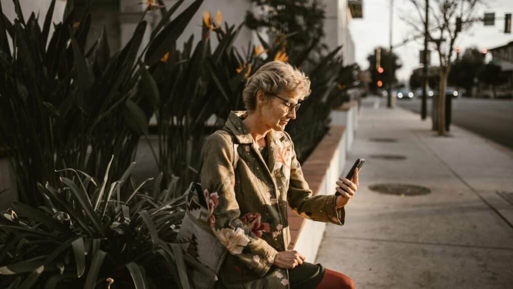 Senior woman sitting outdoors with smartphone, embracing technology in a city setting.