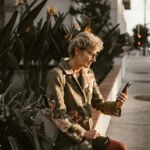 Senior woman sitting outdoors with smartphone, embracing technology in a city setting.