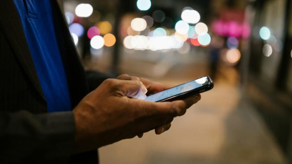 Close-up of a man using a smartphone on a busy city street at night.