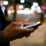 Close-up of a man using a smartphone on a busy city street at night.