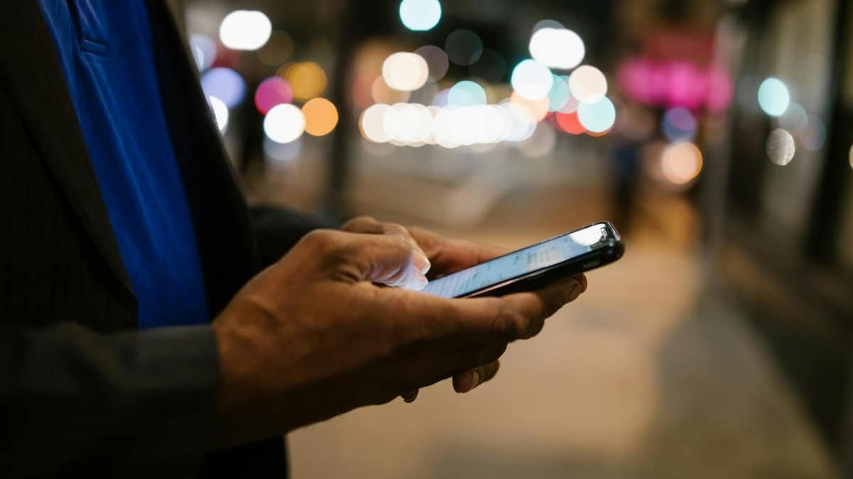 Close-up of a man using a smartphone on a busy city street at night.