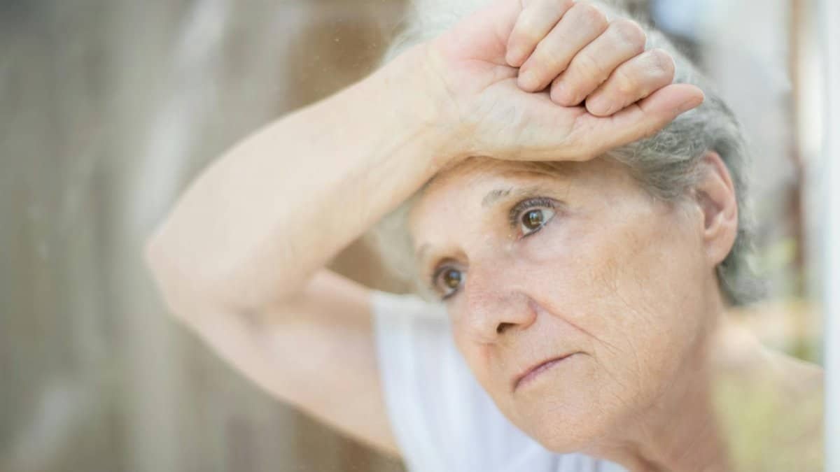 Thoughtful senior woman gazing through a window, symbolizing solitude and reflection.