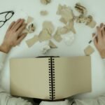 Overhead view of an exhausted man resting with a notepad over his head and crumpled papers around.