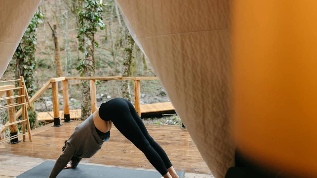 Woman practicing yoga outdoors in a tent, emphasizing relaxation and fitness.
