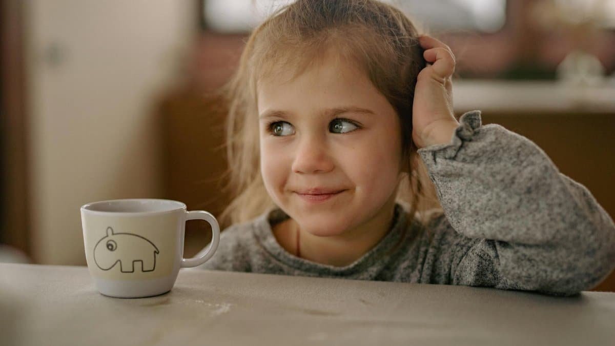 Adorable child smiling indoors, sitting at a table with a cute teacup, creating a cozy atmosphere.