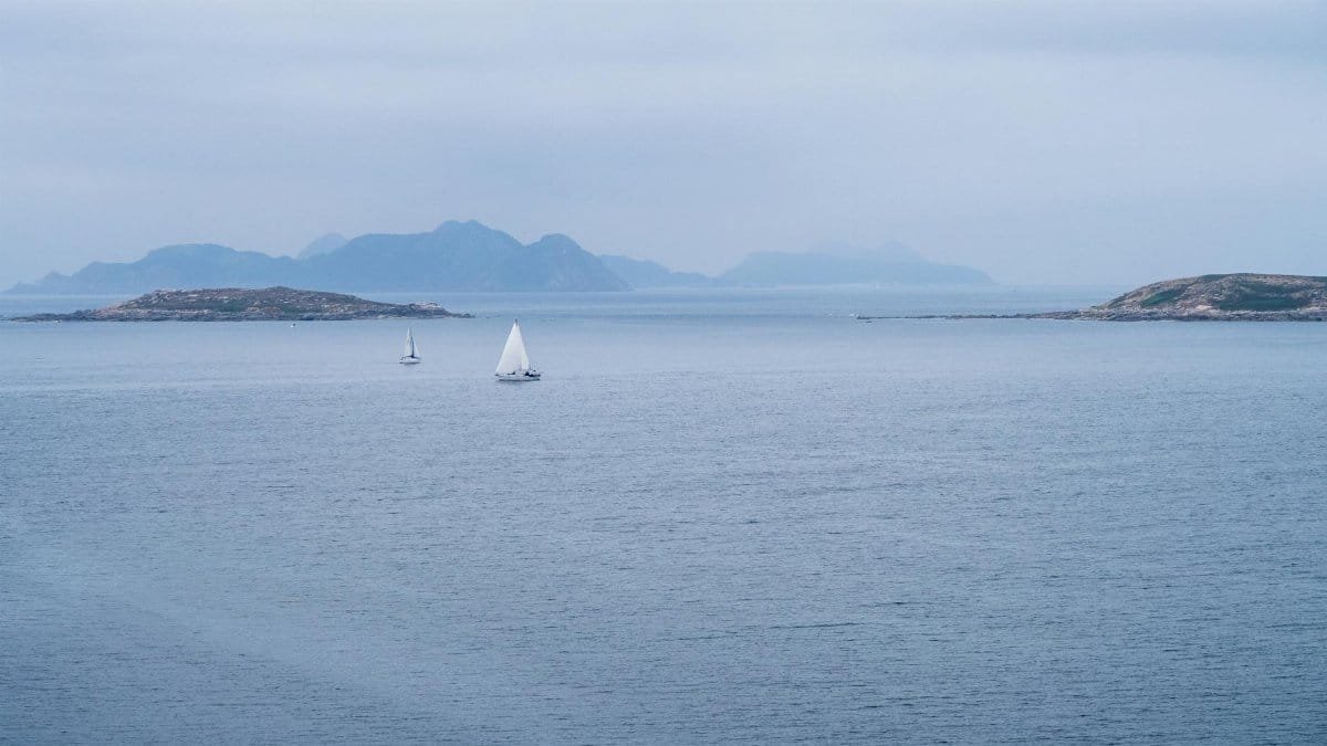 A calm ocean scene with sailboats navigating between remote islands under a blue sky.