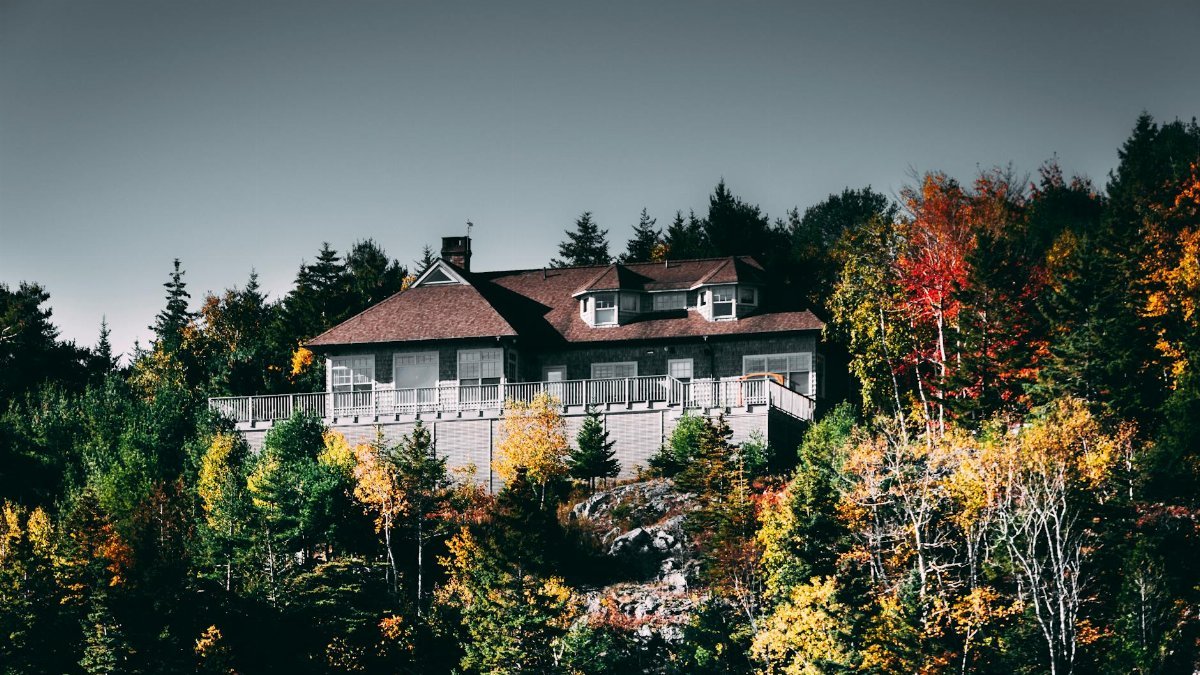 Charming hilltop home surrounded by vibrant autumn forest, showcasing fall beauty in serene countryside.