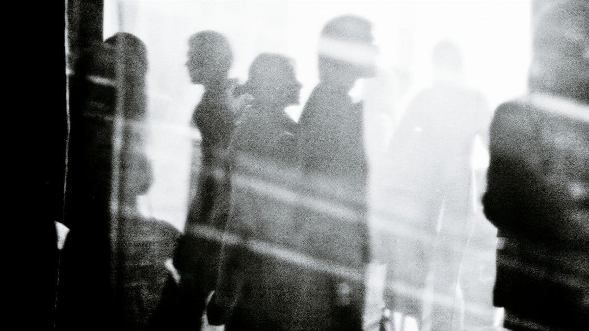 Black and white of crowd of people walking on city street and illuminated by sunlight
