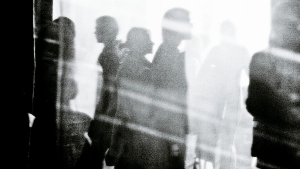 Black and white of crowd of people walking on city street and illuminated by sunlight