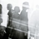 Black and white of crowd of people walking on city street and illuminated by sunlight
