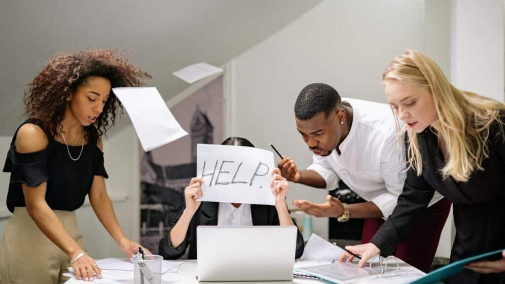 Team of stressed colleagues in an office dealing with paperwork chaos, asking for help.