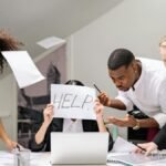 Team of stressed colleagues in an office dealing with paperwork chaos, asking for help.
