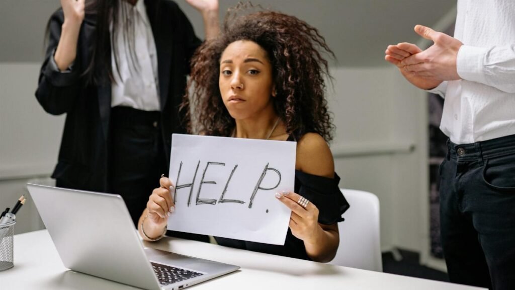 An unhappy businesswoman showing a sign reading 'HELP' in an office setting.
