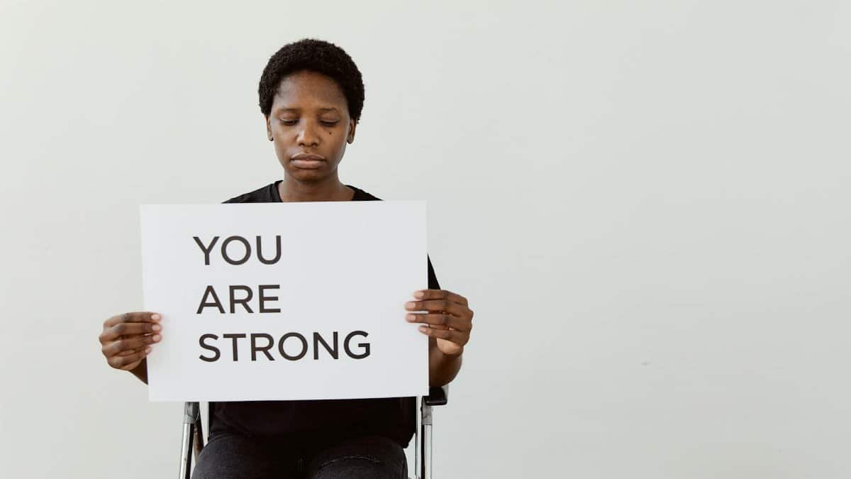 Woman holding 'You Are Strong' sign, promoting empowerment and motivation.