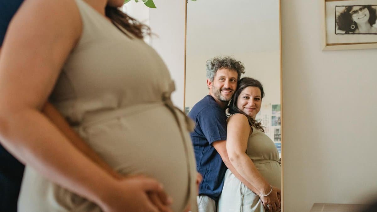 Joyful couple expecting a baby, embracing in front of a mirror indoors.