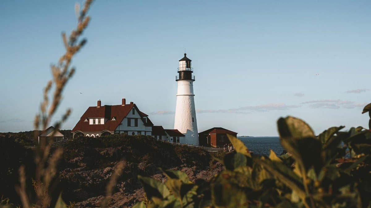 Scenic view of the Portland Head Lighthouse in Cape Elizabeth, Maine against a clear blue sky.