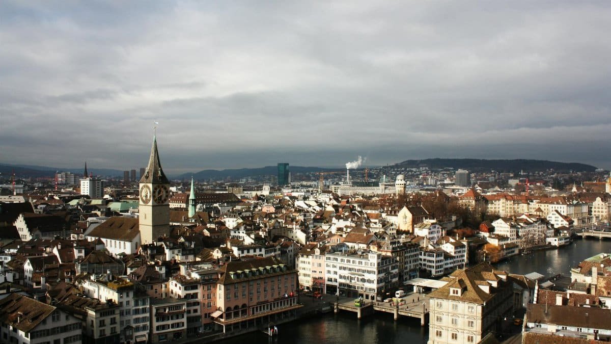 Explore a stunning aerial view of Zurich's historic cityscape with clock towers and canals under a cloudy sky.