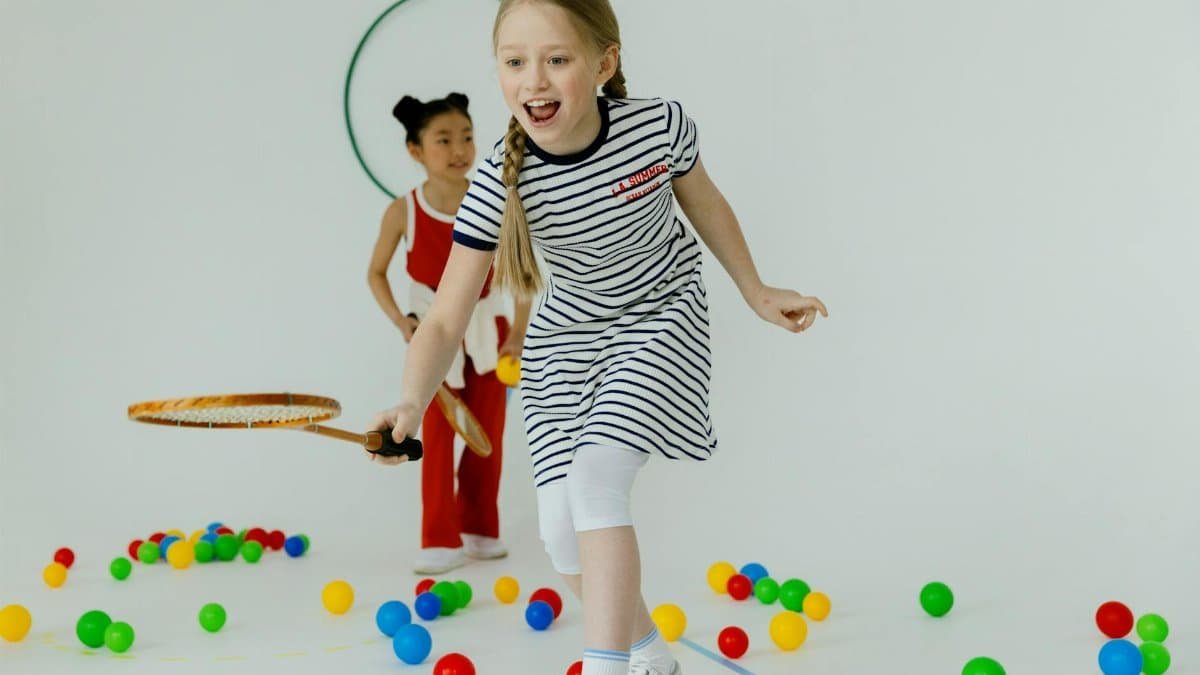 Two girls having fun playing indoors with rackets and colorful balls, full of joy.