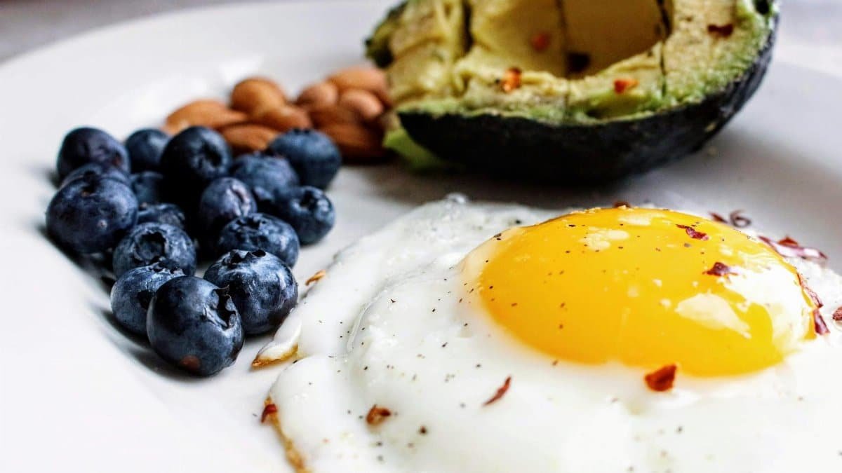 A nutritious breakfast featuring a fried egg, avocado, blueberries, and almonds.
