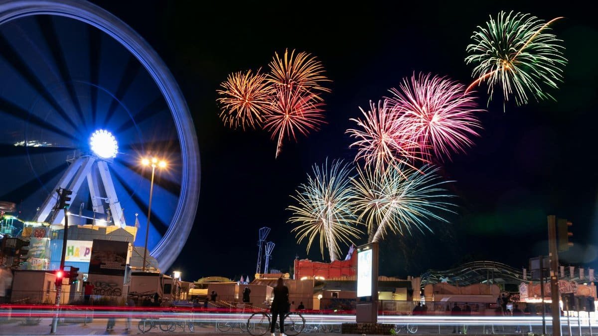Vibrant fireworks illuminate the night sky above a cityscape with a glowing Ferris wheel, capturing the festive atmosphere.