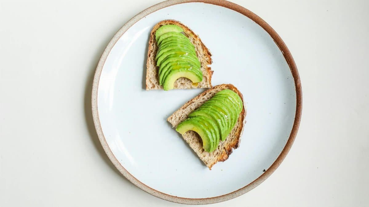 Sliced avocado on whole grain toast presented on a simple plate for a healthy breakfast.