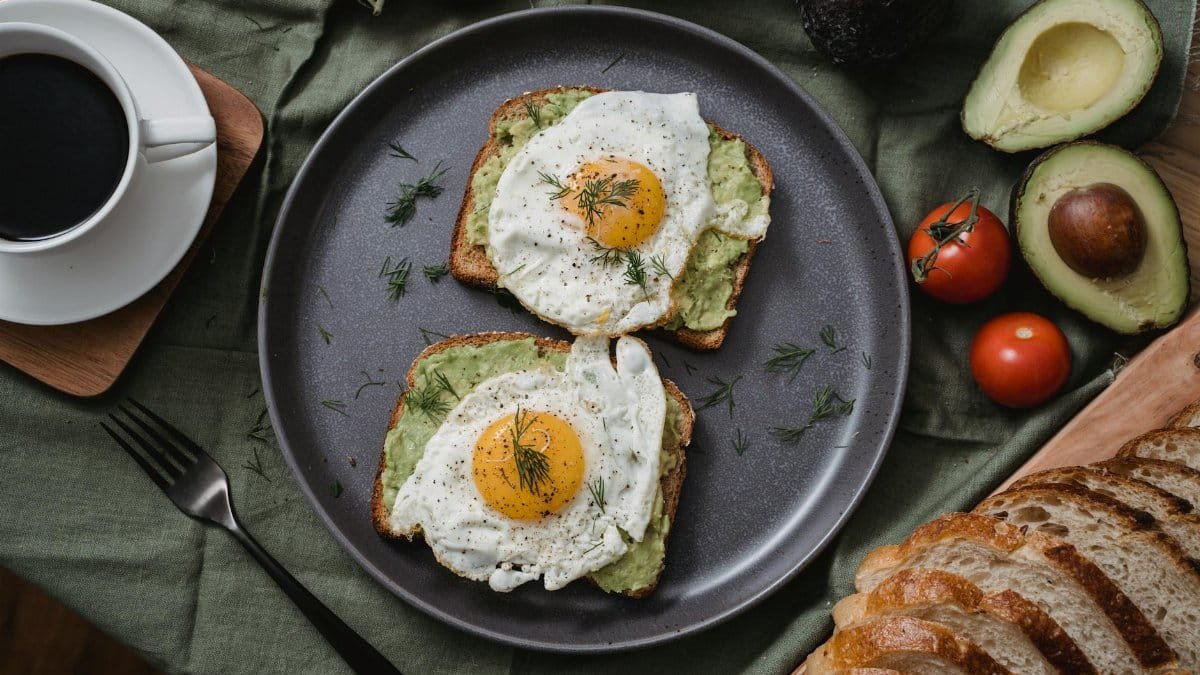 Tasty avocado toast topped with sunny side up eggs, served with a cup of coffee.