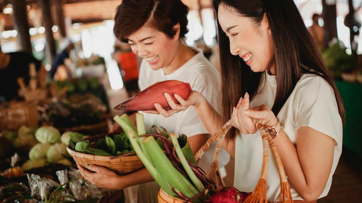 Asian women enjoying organic produce shopping at a lively local market, embracing fresh, healthy living.