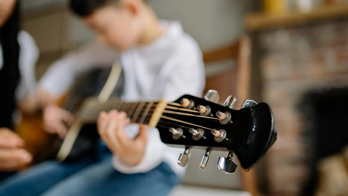 A young child learning to play the acoustic guitar indoors, focused on the fretboard.