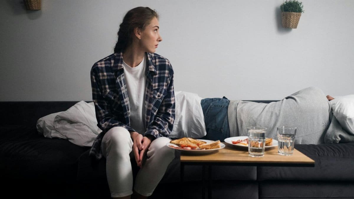 Woman in casual wear seated on sofa with breakfast in cozy room.
