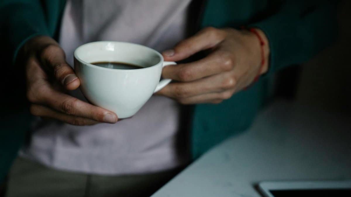 Close-up of hands holding a warm cup of coffee indoors, creating a cozy atmosphere.