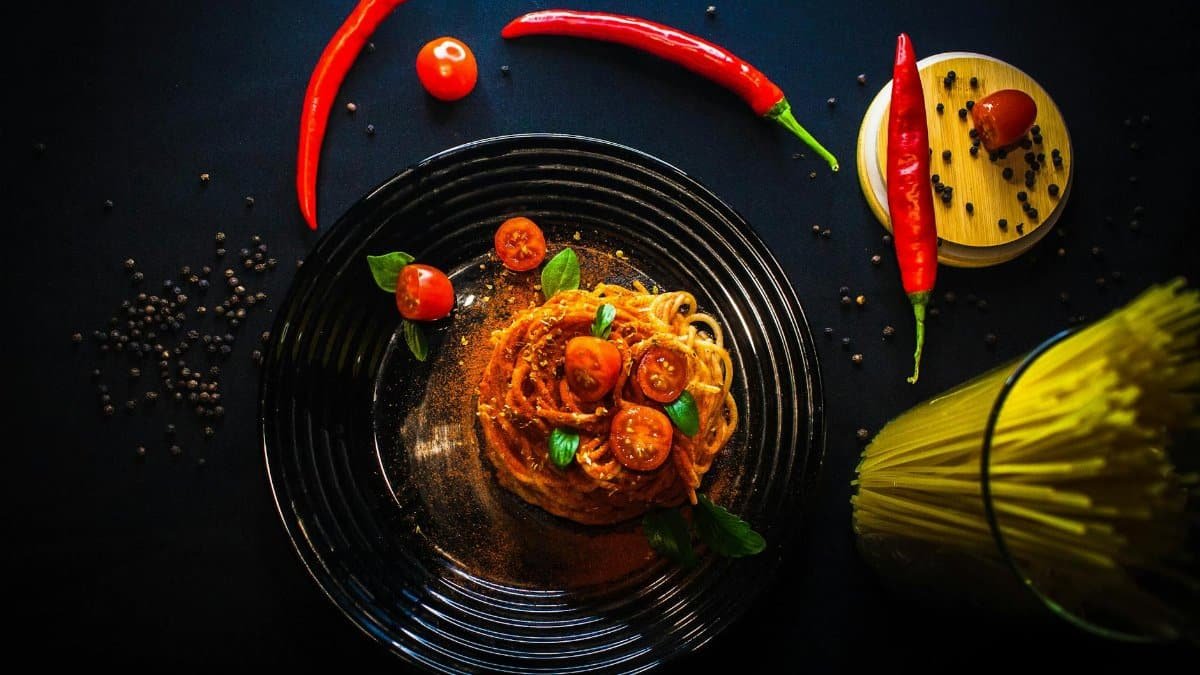 Tantalizing overhead shot of spaghetti aglio olio with cherry tomatoes, chili peppers, and spices on a dark background.