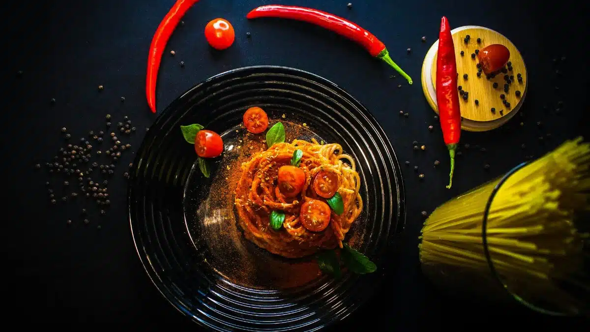 Tantalizing overhead shot of spaghetti aglio olio with cherry tomatoes, chili peppers, and spices on a dark background.