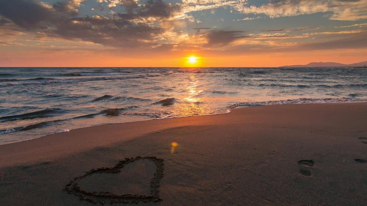 Beautiful sunset over ocean with a heart shape in the sand, perfect for romantic themes.
