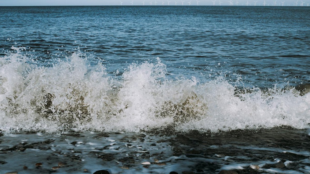 Captivating shot of waves crashing with offshore wind turbines on the horizon.