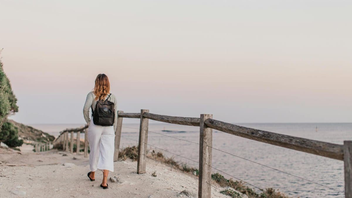 A woman walks along a scenic coastal path, enjoying a tranquil sunset view by the sea.