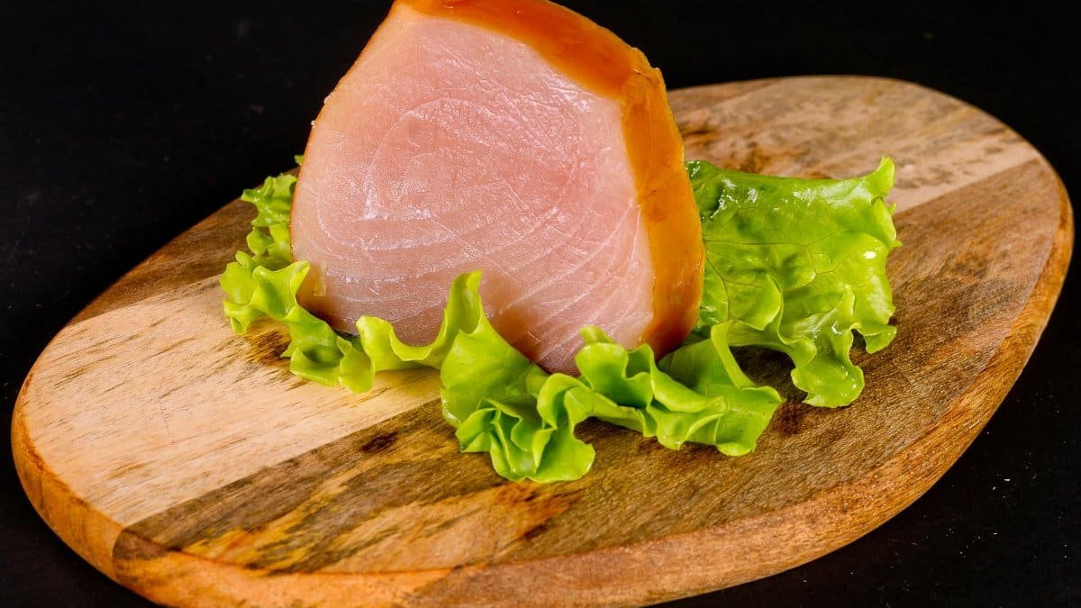 Close-up of fresh sliced ham on a wooden board with lettuce, perfect for food presentation.