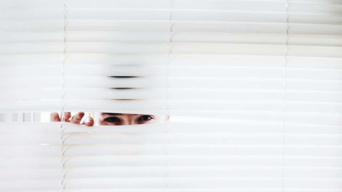 A person peeks through white blinds, creating an intriguing sense of curiosity.