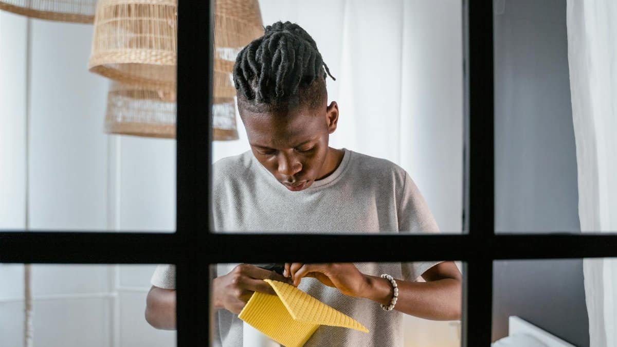A young man indoors cleaning with a yellow sponge, concentrating on his task.