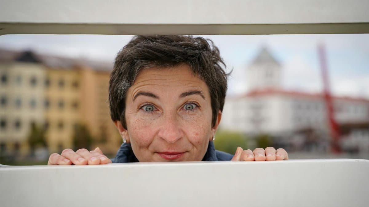 Smiling woman peeks through a fence in Jelgava, Latvia, embracing curiosity and joy.
