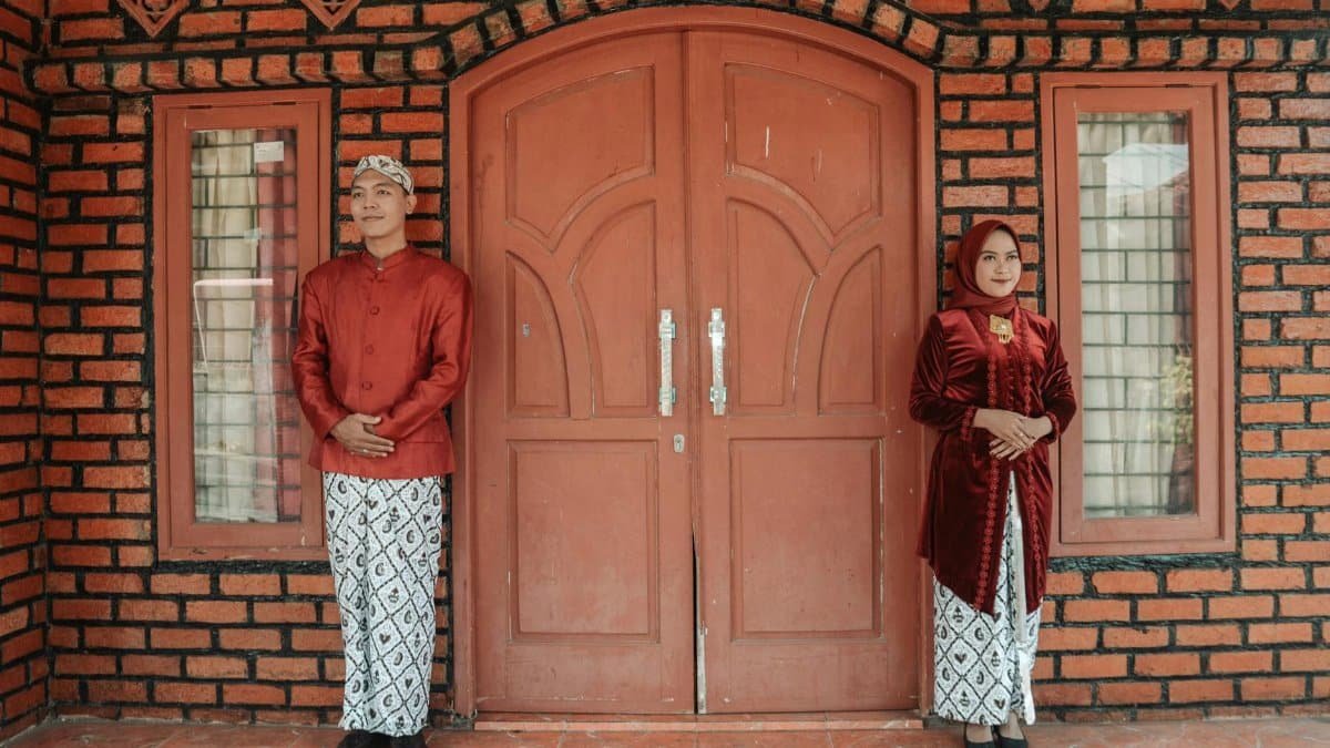 Asian couple in traditional attire posing by a beautiful brick wall and door.